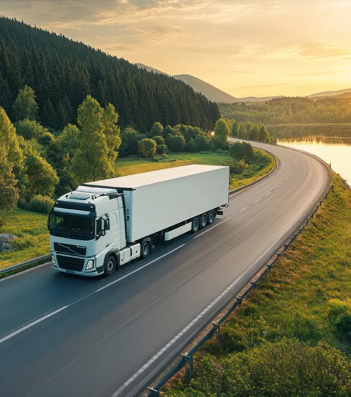 Biały samochód ciężarowy jadący płynnie malowniczą trasą wzdłuż jeziora. W biznesie transportowym liczy się ciągłość łańcucha dostaw. Chronimy floty samochodowe i przewoźników. Dobrze dobrane pakiety OC, AC i OC przewoźnika gwarantują, że jedna losowa kolizja lub awaria w trasie nie zatrzyma Twojej firmy i nie zrujnuje budżetu.